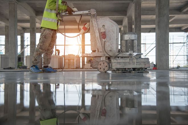 Worker using a floor grinder on a concrete surface in a bright construction site