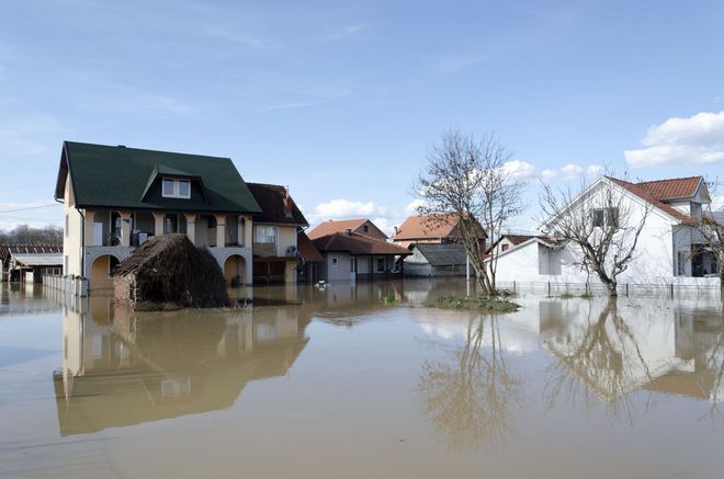 Flooded residential street with houses partially submerged in muddy water under a clear sky
