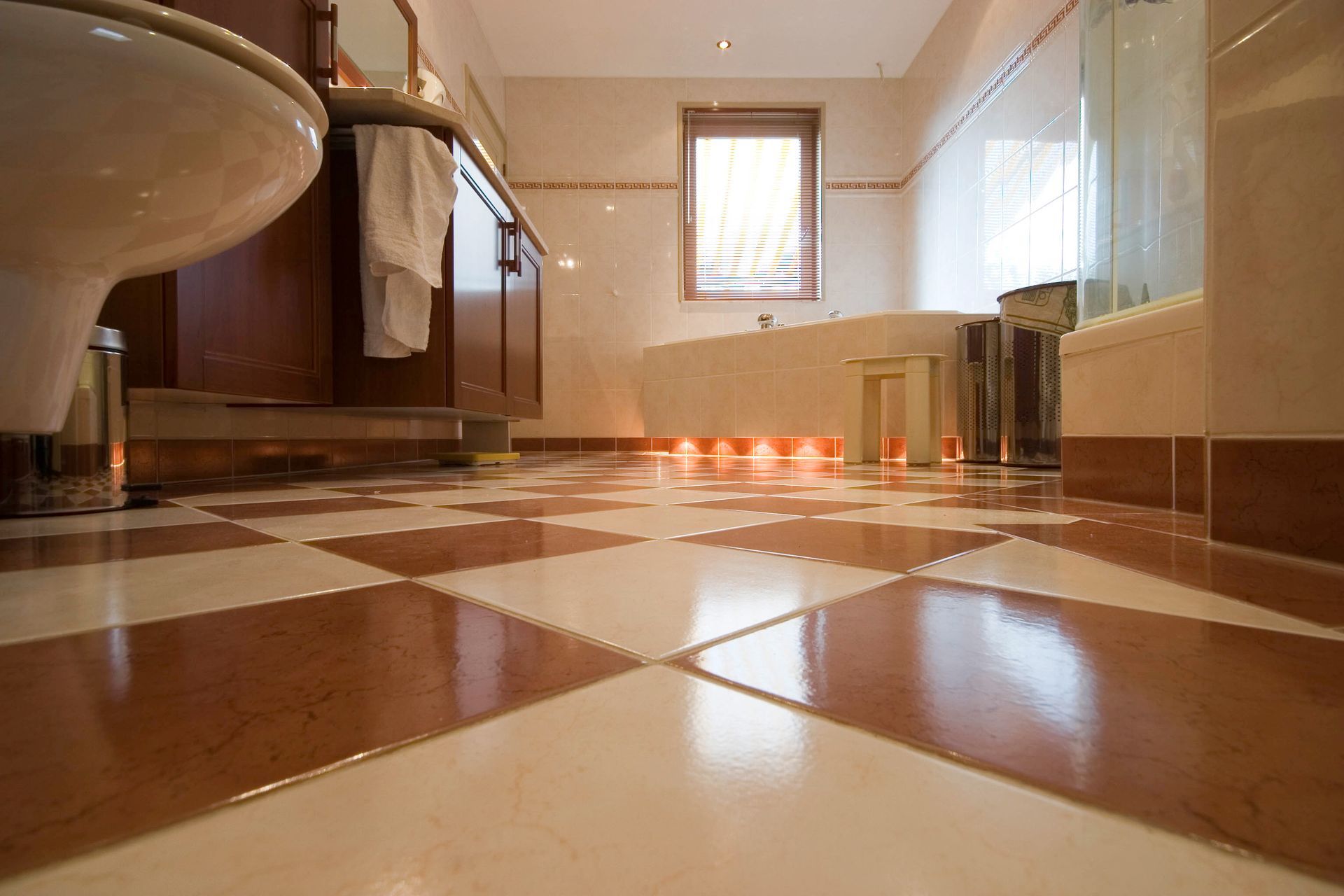 Bathroom with checkered brown and cream tiles, toilet, wooden vanity, and a window.