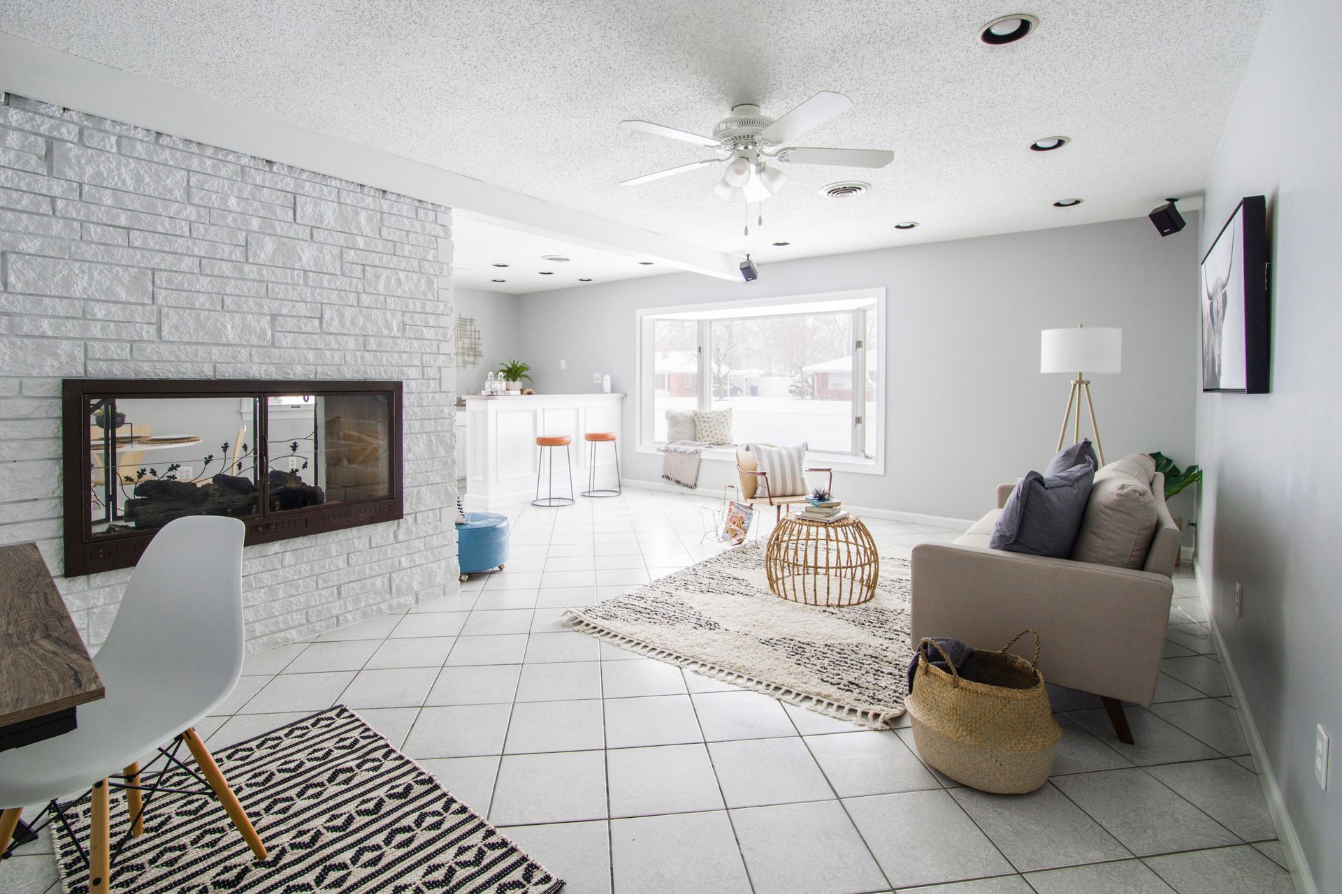 Living room with white brick fireplace, modern furniture, and a rug on white tile flooring.