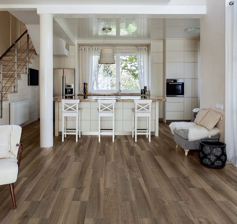 Modern kitchen with wood floors, white island with chairs, open to living area with stairs.