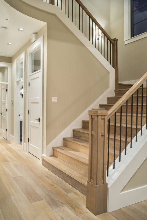 Wooden staircase with black railings, beige walls, and white trim in a modern home.