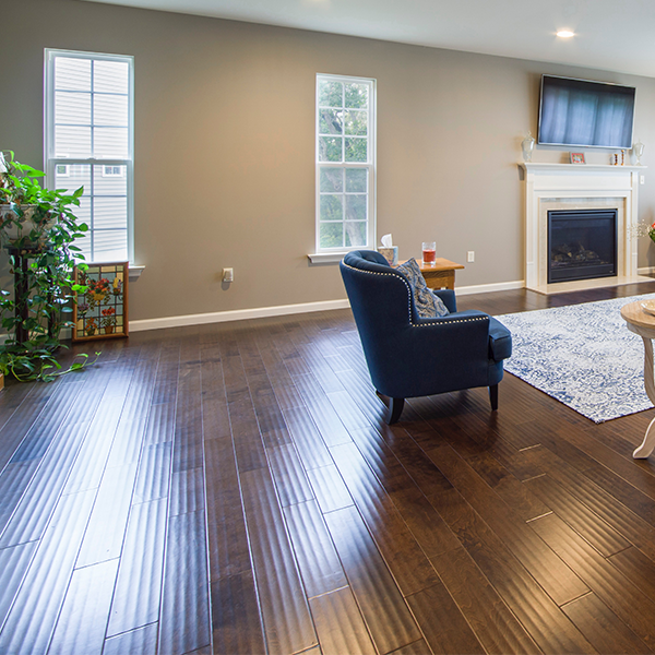 Living room with dark wood floors, blue armchair, fireplace, and two windows.