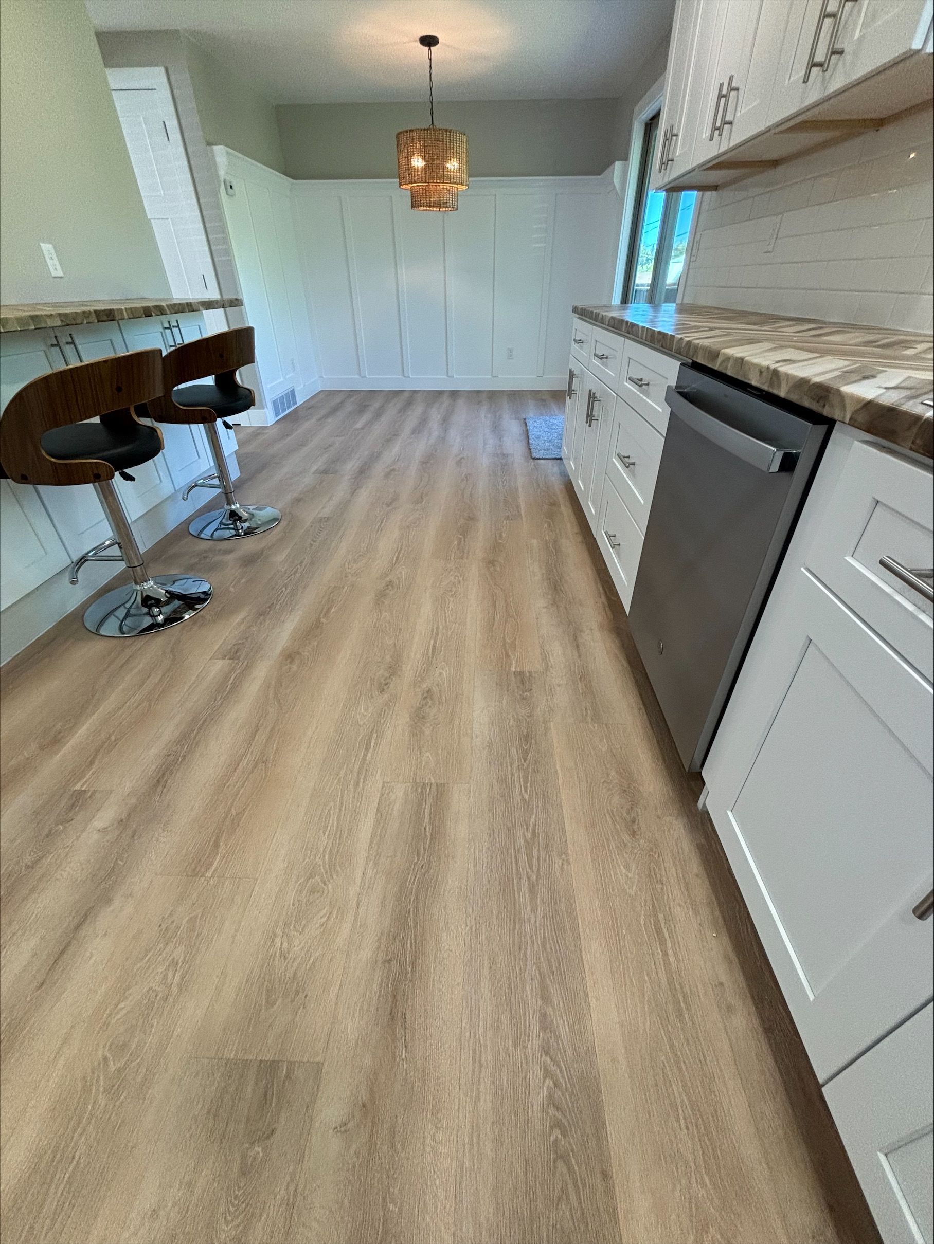 Kitchen with wood-look flooring, white cabinets, stainless steel appliances, and a hanging light fixture.