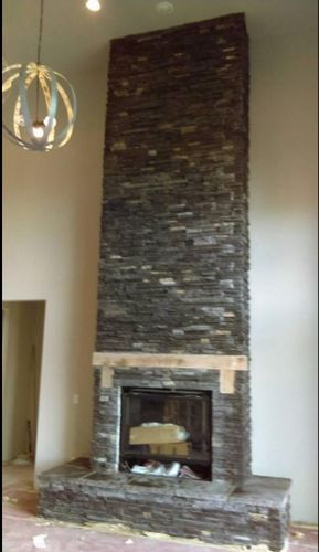 Stone fireplace in a home with wood mantel and matching hearth. Tall and narrow.