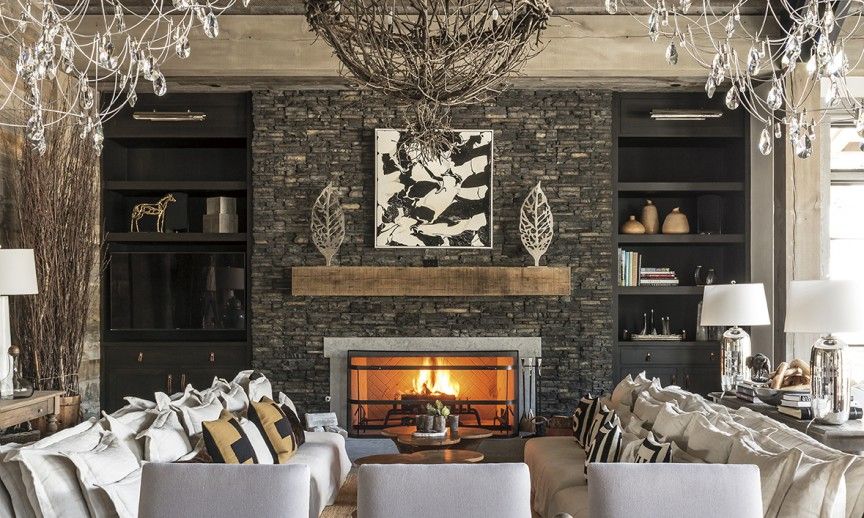 Living room with fireplace, stone wall, built-in shelves, couches, and crystal chandeliers.