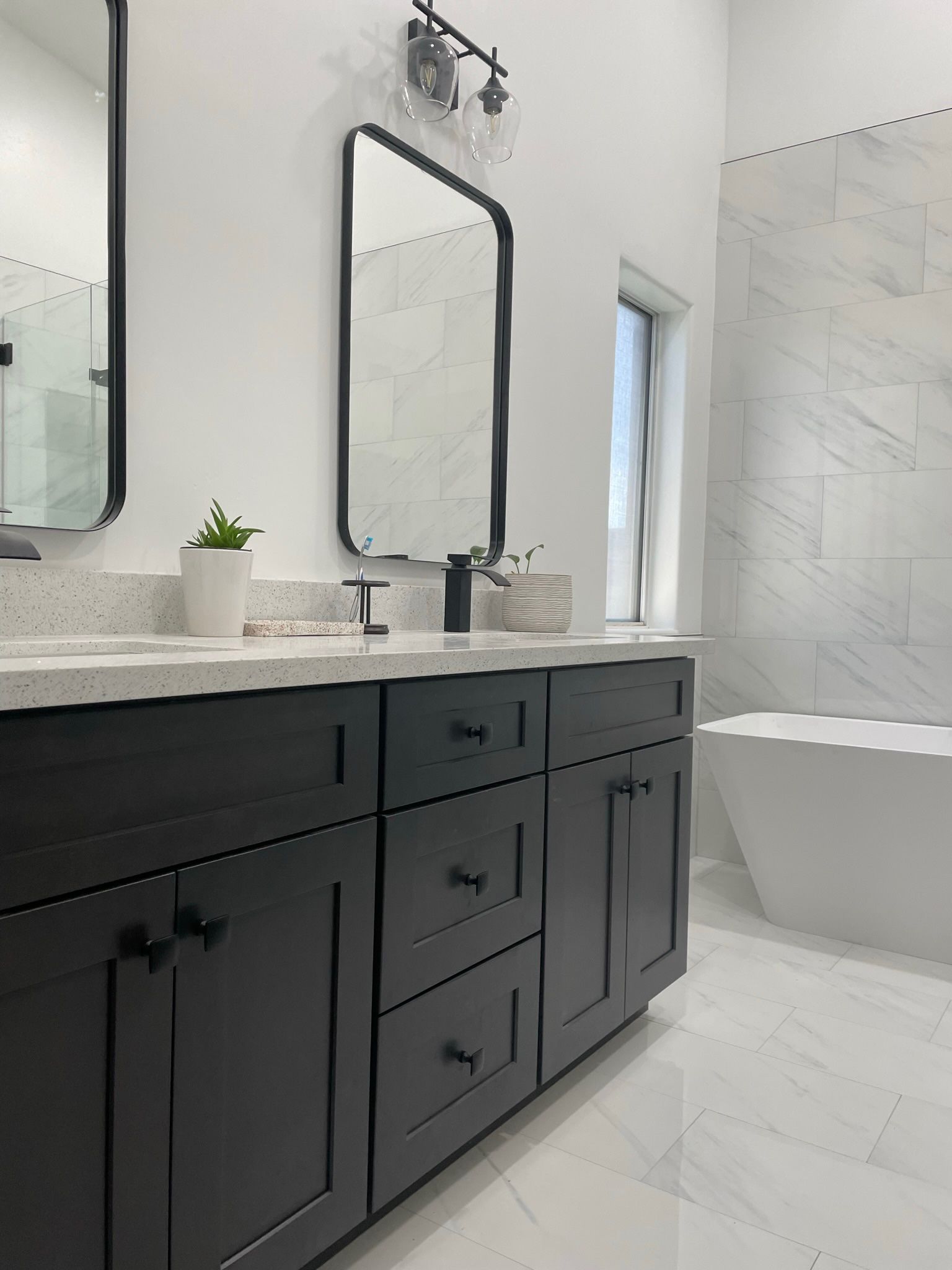 Modern bathroom with black vanity, white countertops, marble shower, and freestanding tub.