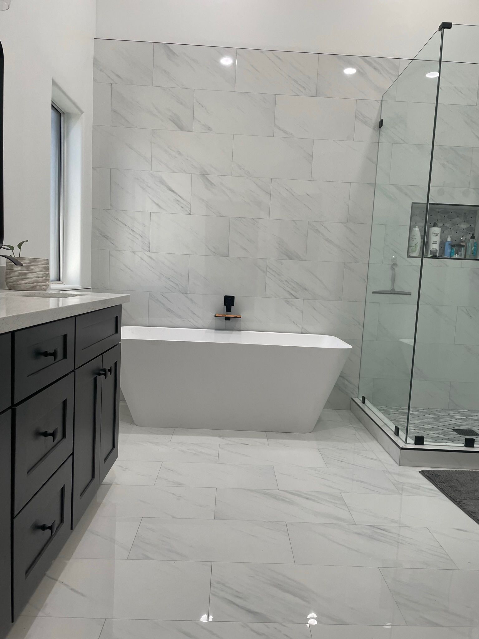 Modern bathroom with white marble tile, gray vanity, and glass shower.