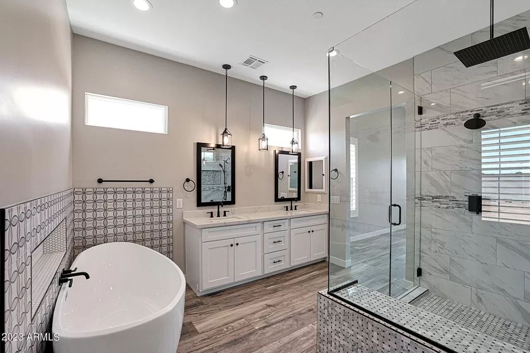 Modern bathroom with white cabinets, freestanding tub, glass shower, and marble tile.
