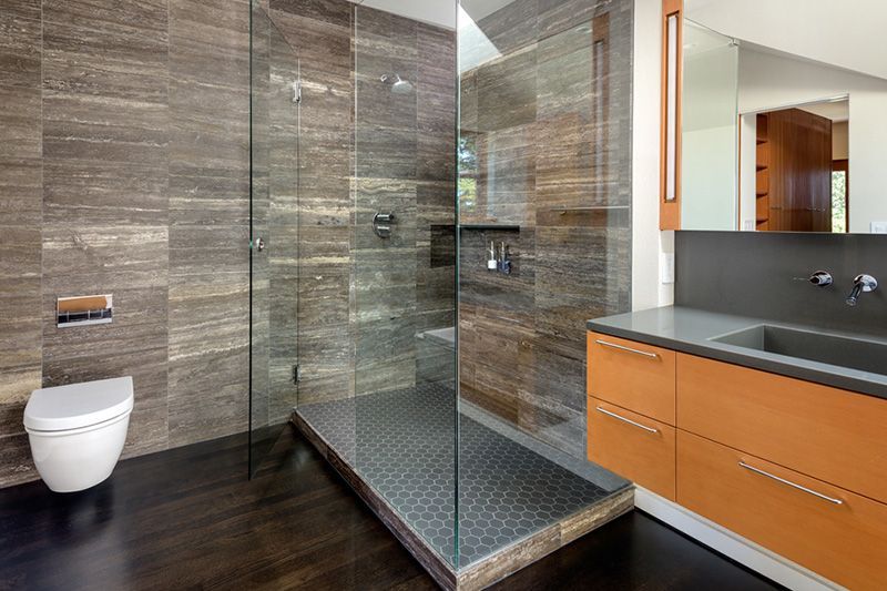 Modern bathroom with walk-in shower, dark wood floors, gray tile walls, floating vanity, and a toilet.