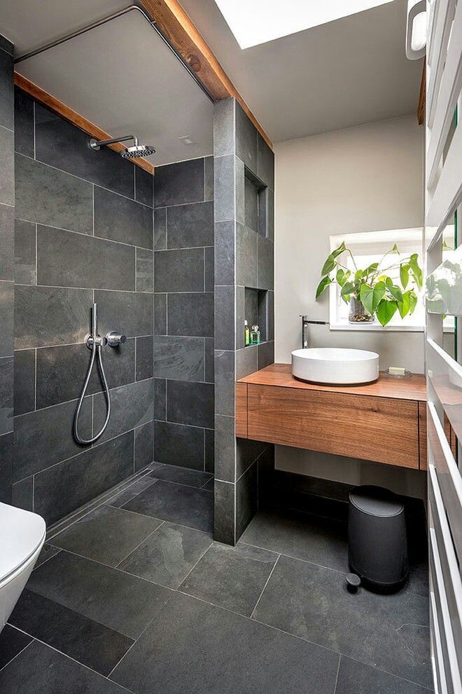 Modern bathroom with slate tile shower, floating wooden vanity, and skylight.