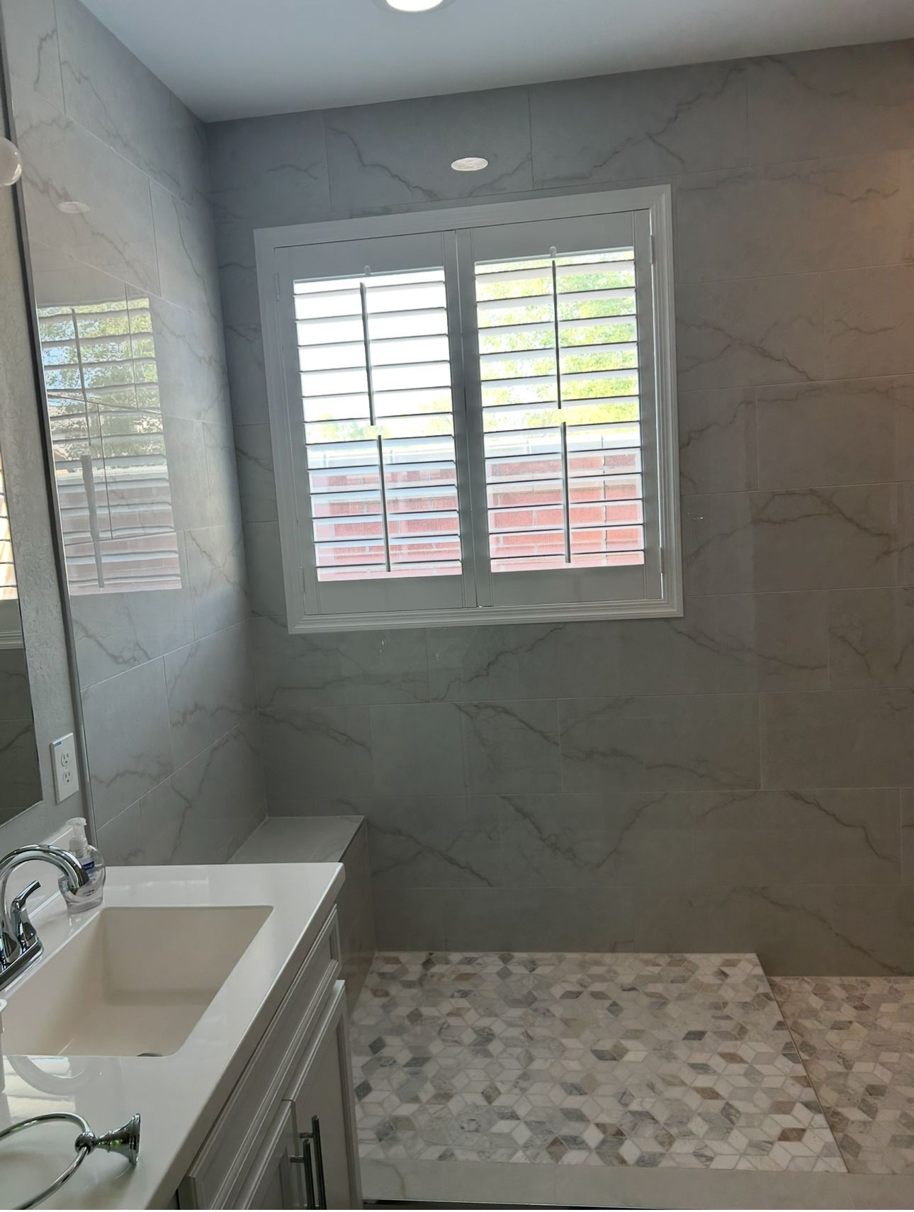 Bathroom with white shutters, marble tile walls, and a white sink.