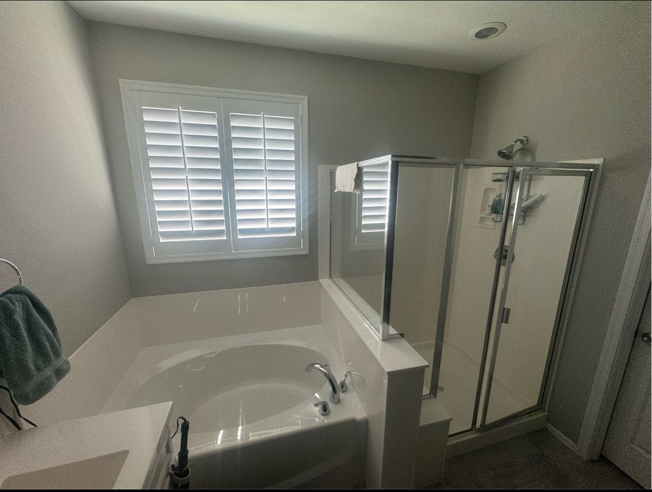 Bathroom with tub, shower, and window with shutters. White walls and light-colored fixtures.