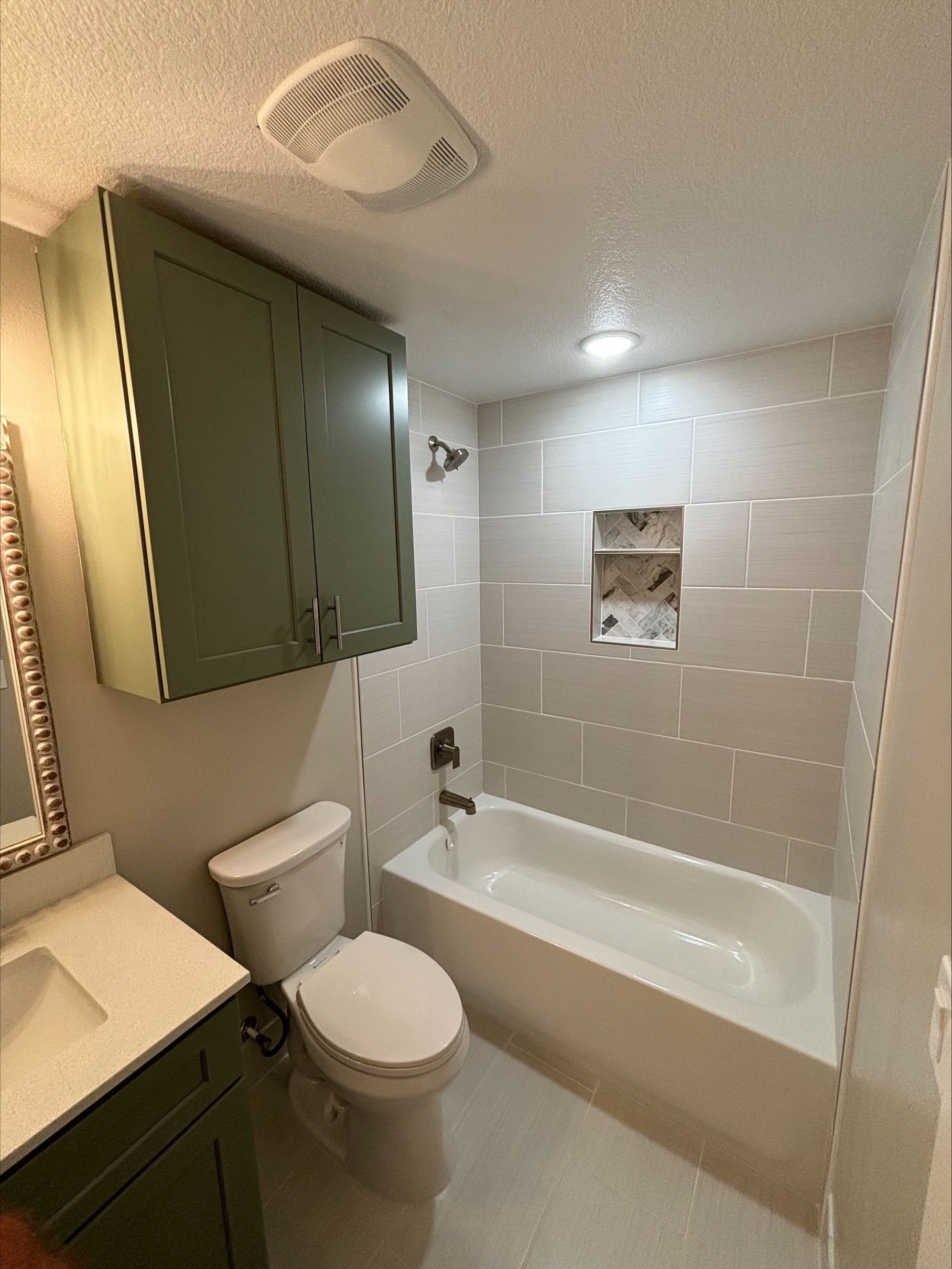 Bathroom with sage green cabinets, white fixtures, and tiled shower.