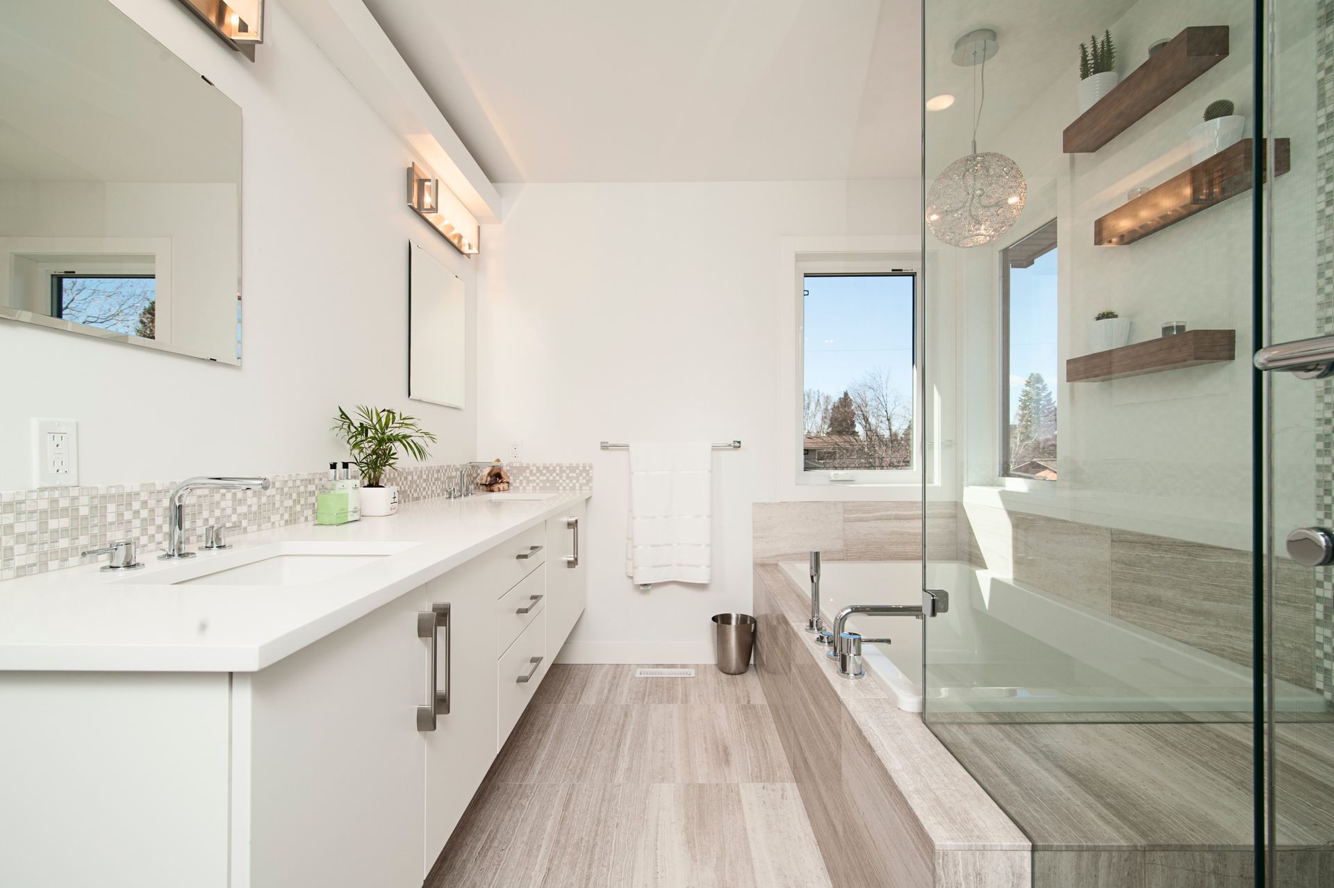 Modern white bathroom with double vanity, bathtub, and large glass shower.