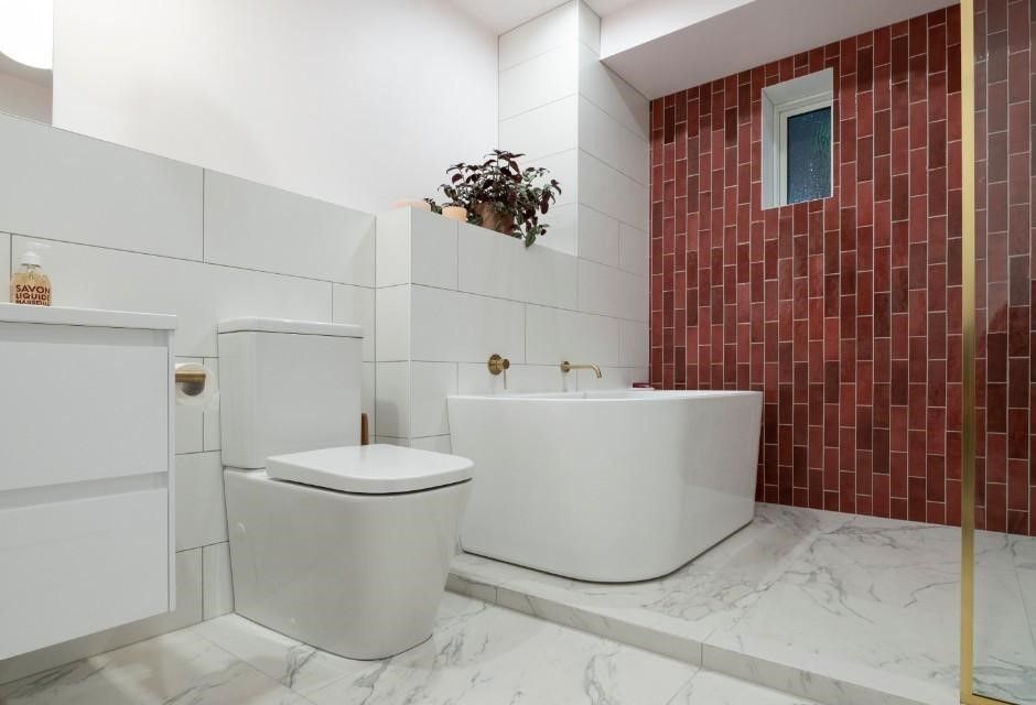 Modern bathroom with white and red brick tiles, a white tub, toilet, and vanity. Marble flooring.
