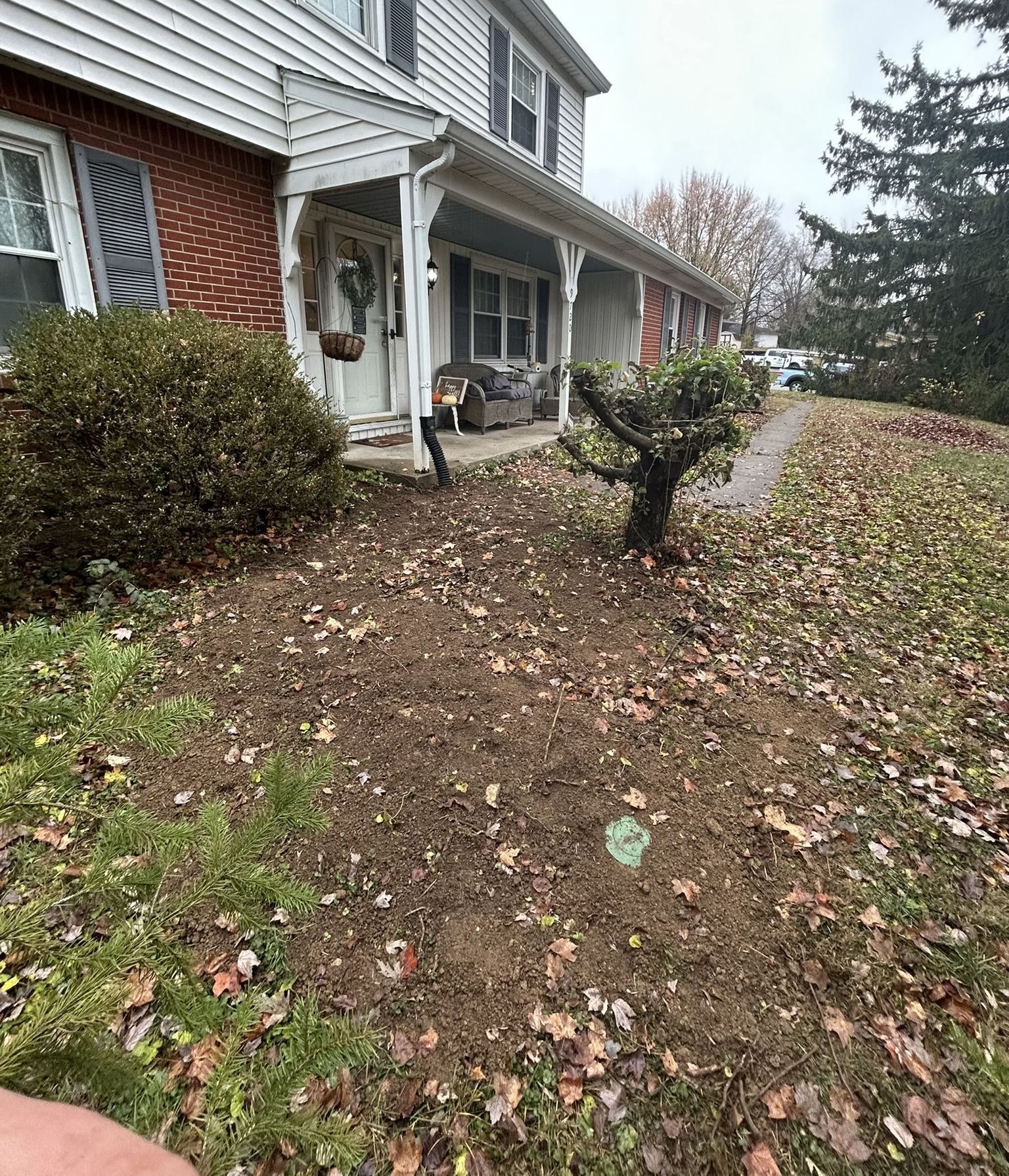 Two-story house with detached porch, yard covered in leaves and dirt.