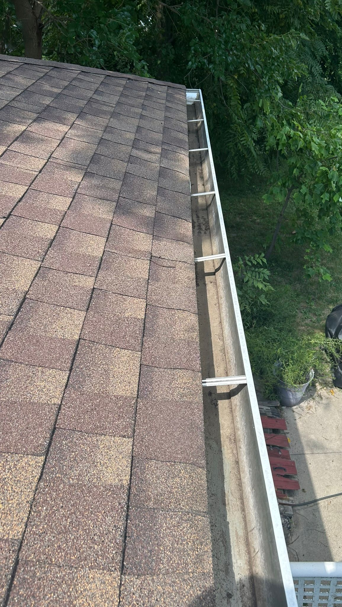 Roof with brown shingles and a gutter, trees in background.