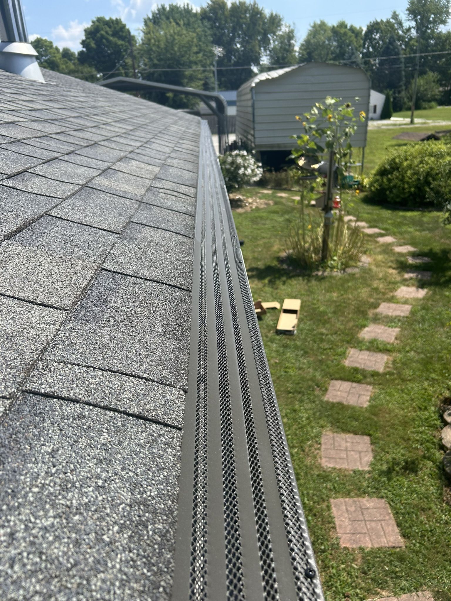 A roof with gray shingles and a gutter with a mesh guard, viewed from the side, outdoors.
