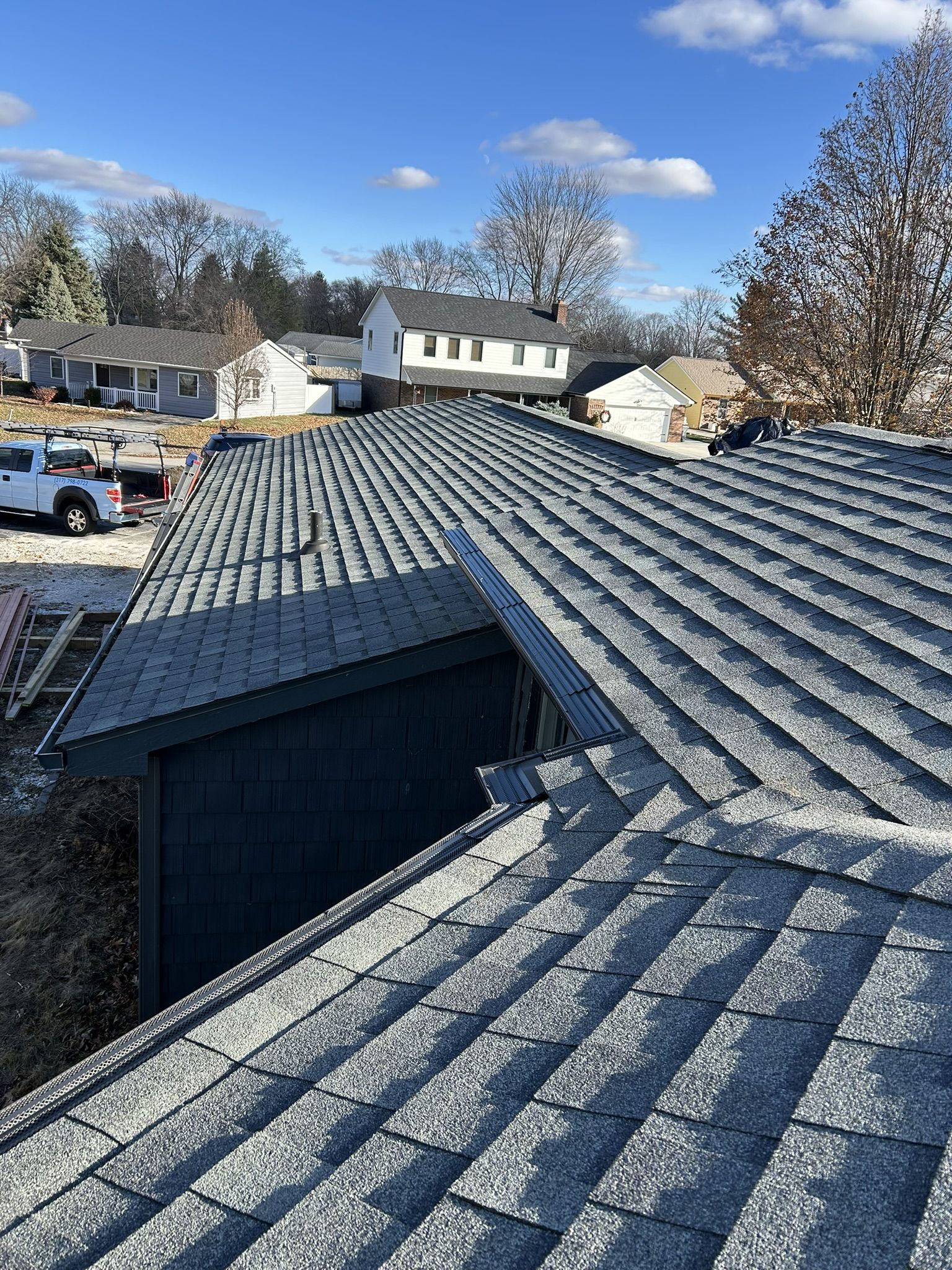 Gray shingled roof with a clear blue sky, other houses, and a truck in the distance.