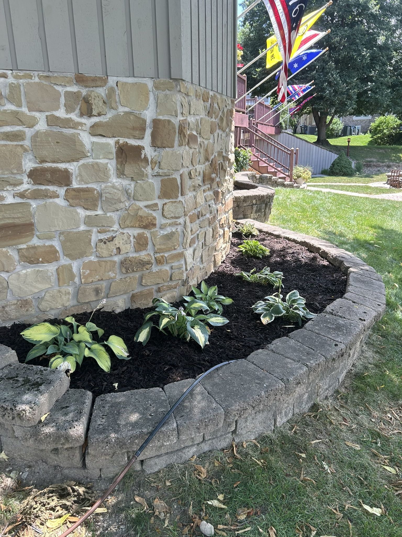Stone building corner with flower bed and flags in the background.