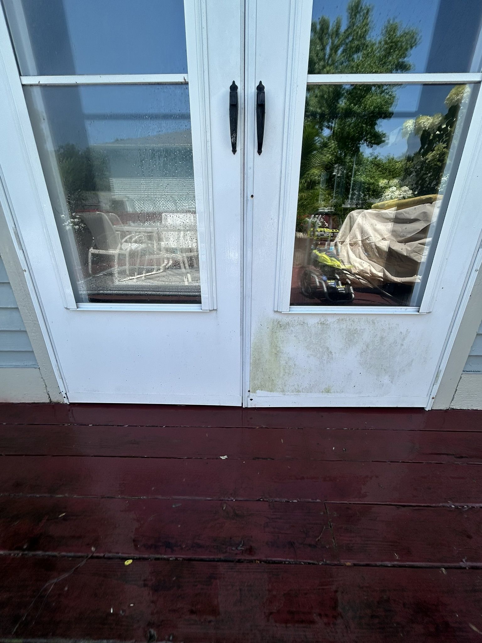 White French doors with green staining and black handles, opening onto a red-stained wooden deck.