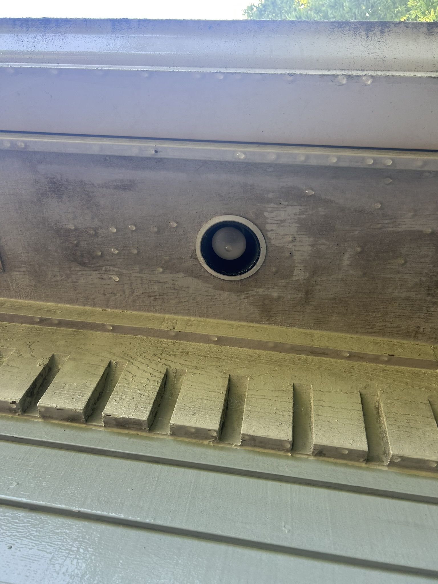 Close-up of a dark drain opening in a painted metal surface. Below it is a decorative, light-colored ledge.
