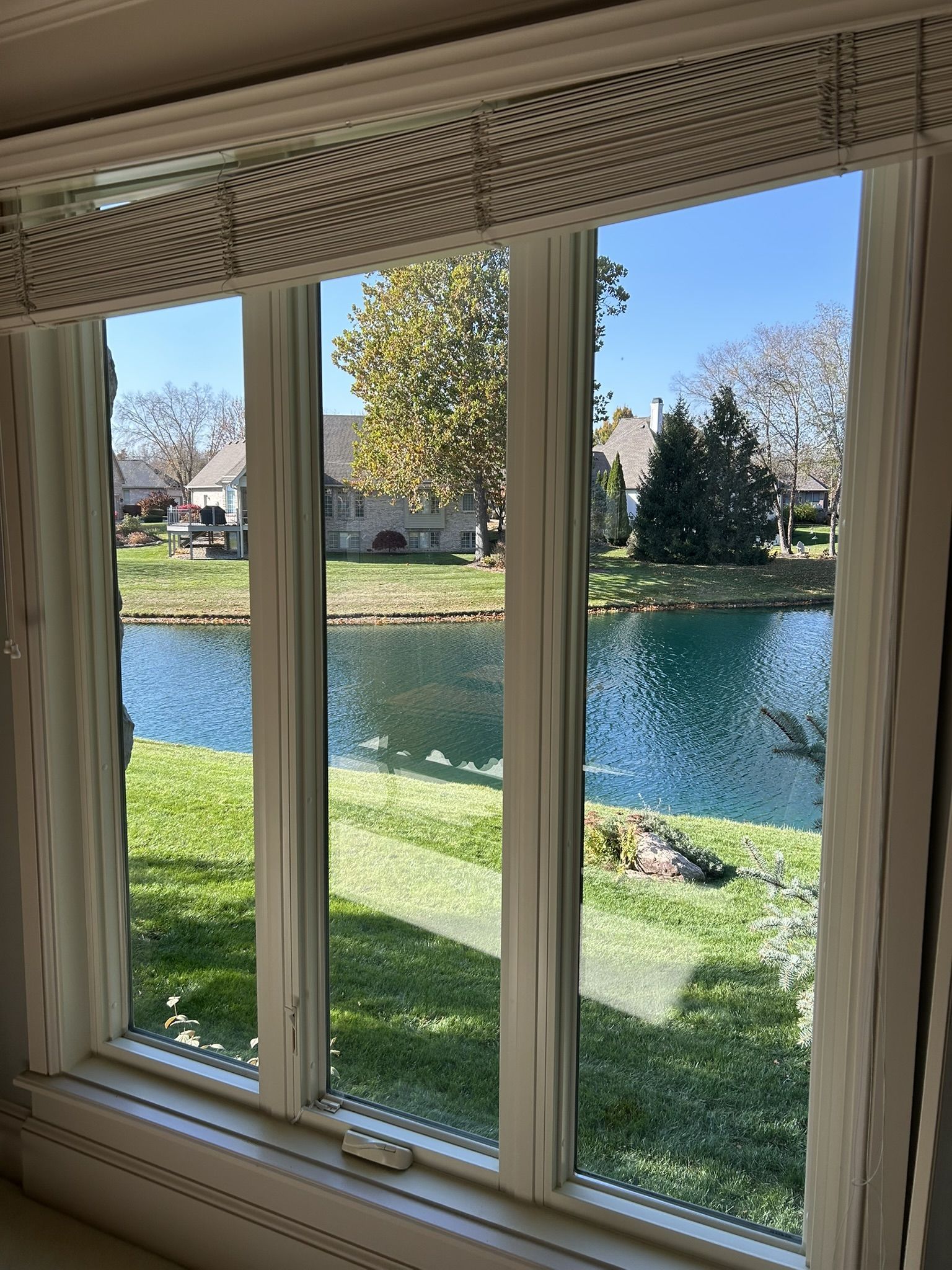View through a window overlooking a pond and yard with houses in the background on a sunny day.