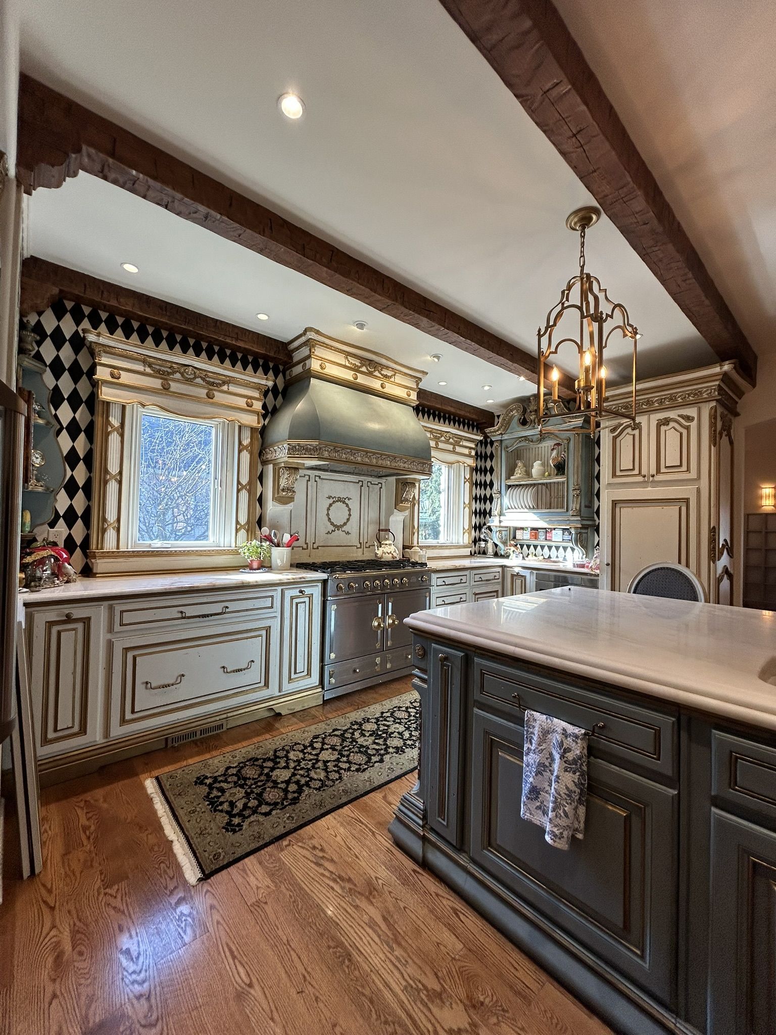 Elegant kitchen with gray and gold cabinetry, wood beams, and a large central island.