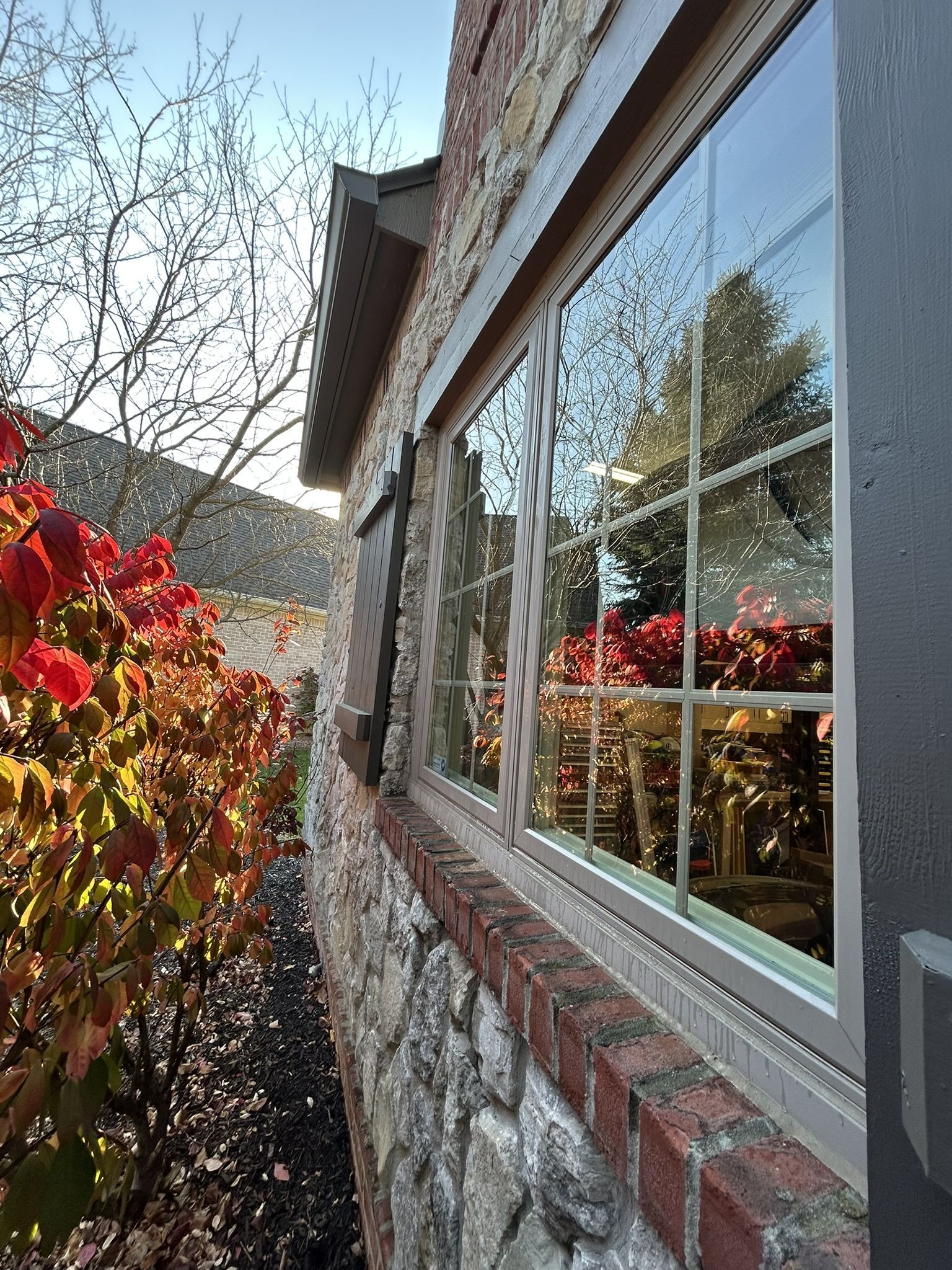 Stone house with window reflecting autumn foliage and a mountain backdrop.
