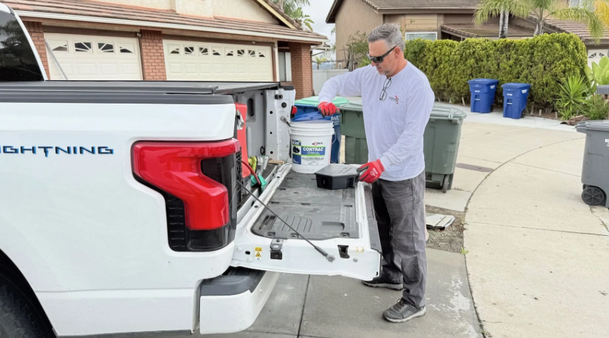 A person in a long-sleeved shirt and gloves organizing tools on the lowered tailgate of a white Ford Lightning truck.