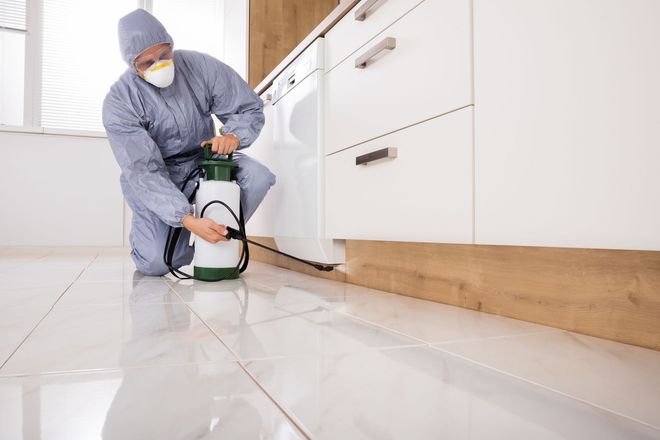 Worker cleaning a white tile floor with a floor scrubber in a kitchen.