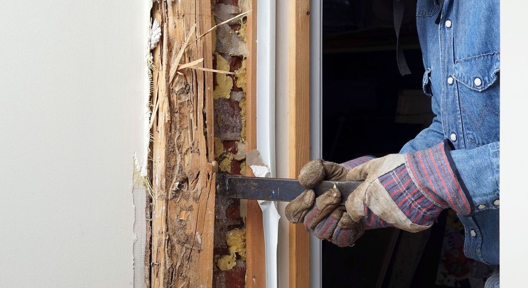 Person using a pry bar to remove rotted wood from a door frame during termite pest control services.