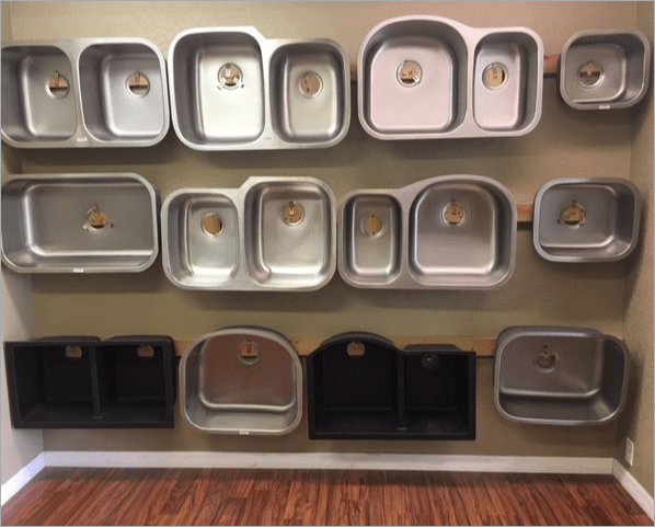 Various stainless steel and black kitchen sinks displayed on a wall.