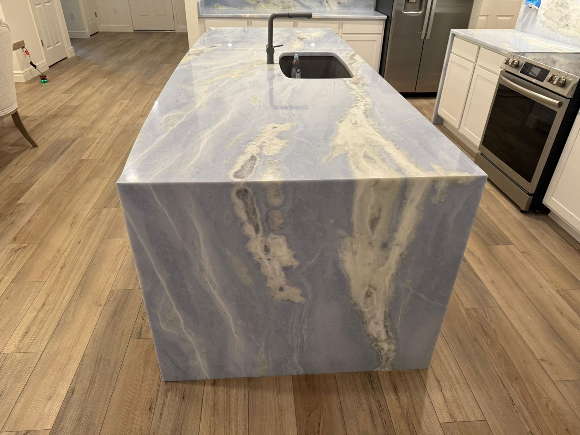 Blue and white veined marble countertop on a kitchen island with a black faucet and sink.
