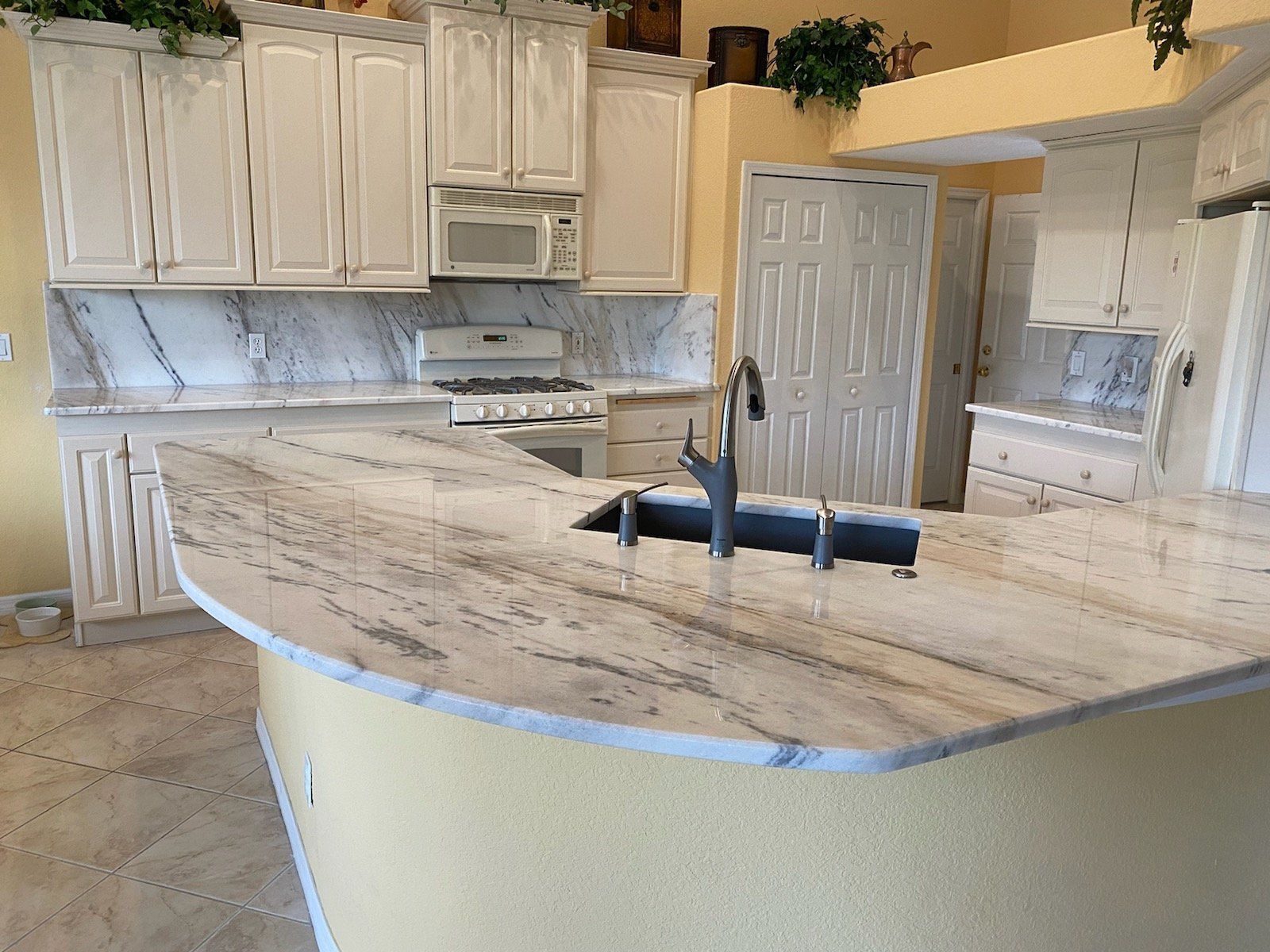 Kitchen with cream-colored cabinets and countertops, featuring a curved island with a sink.
