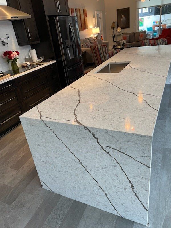 Modern kitchen with white countertop, dark veining, and a built-in sink. Black cabinets and appliances.
