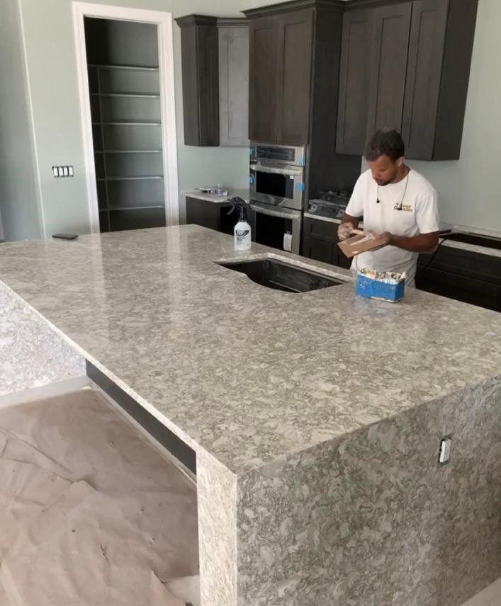 Man working on a light-colored countertop in a kitchen with dark cabinets, a built-in oven, and pantry.