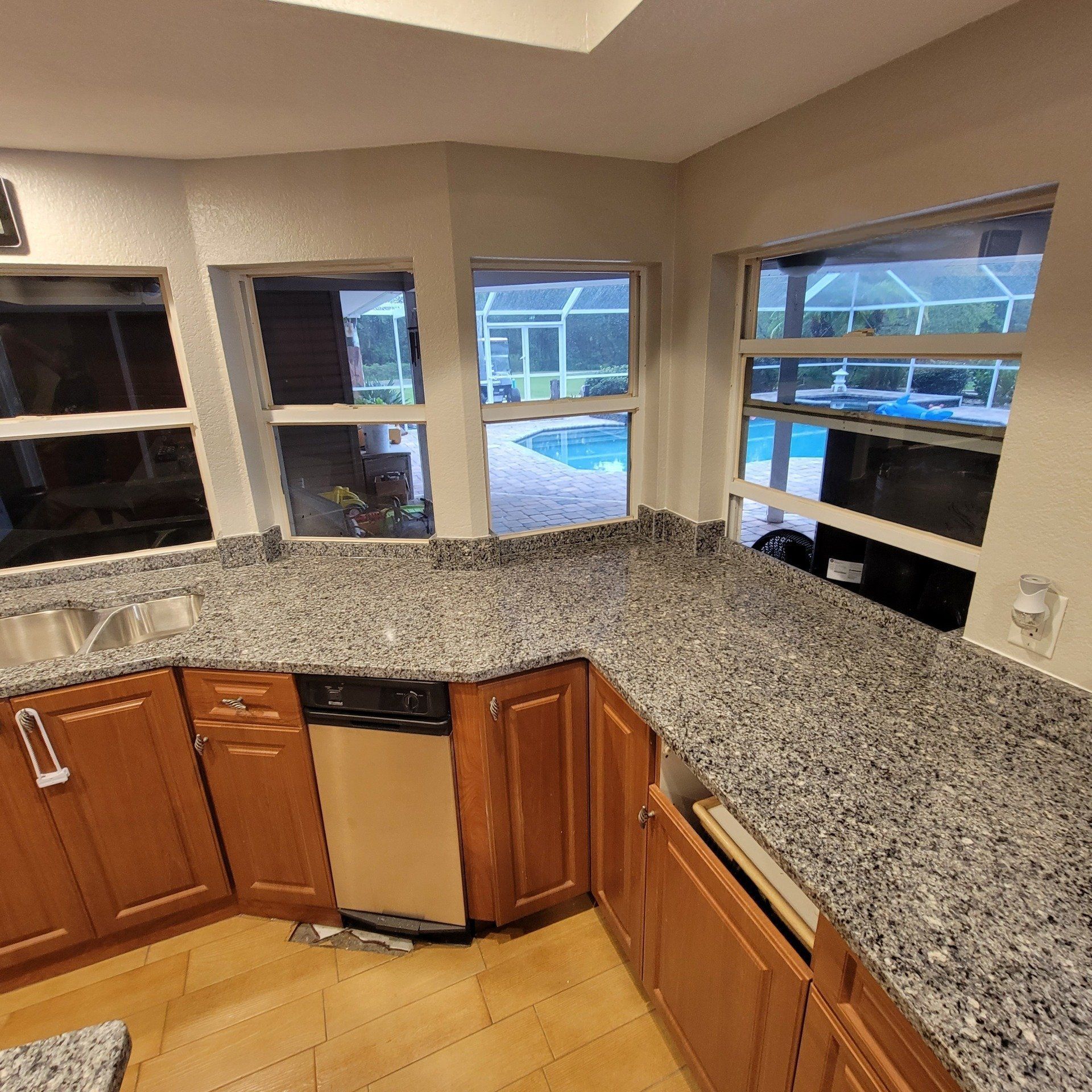 Kitchen with granite countertops and wooden cabinets, windows overlooking a pool.