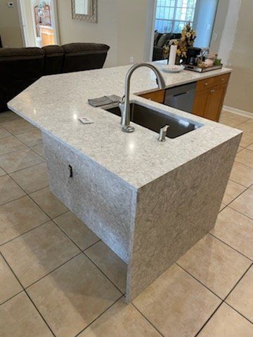 Kitchen island with light-colored countertop, sink, and faucet. Granite-like texture on the sides; tile floor.