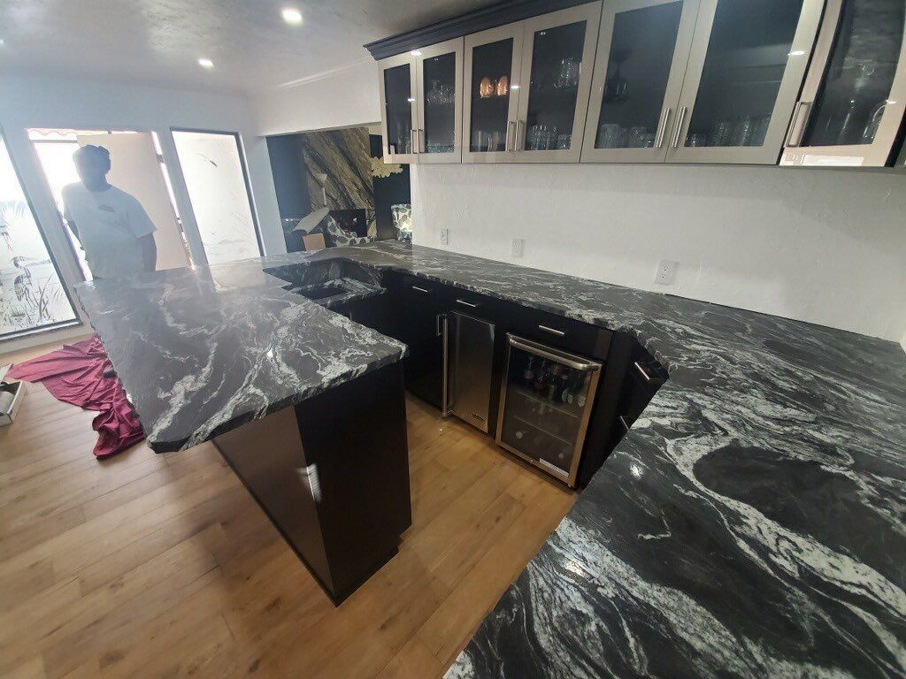 A modern kitchen with black granite countertops, cabinets, and a built-in wine fridge.