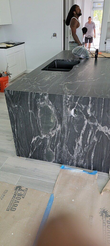 A kitchen with a dark countertop and people in the background. Construction in progress.