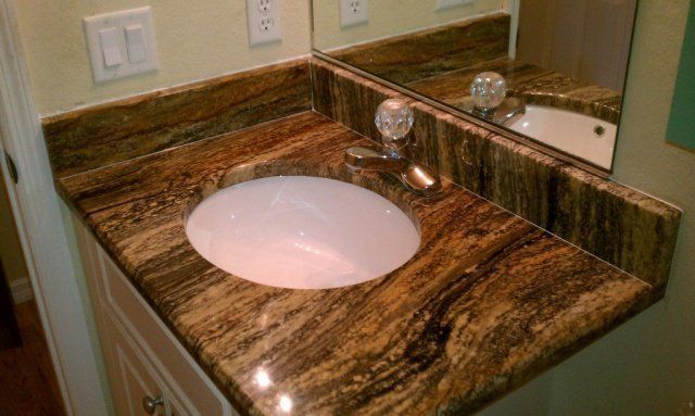 Bathroom vanity with brown granite countertop, white sink, and decorative faucet.