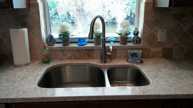 Kitchen sink with a window, countertop, and faucet, with flowers and a paper towel holder.