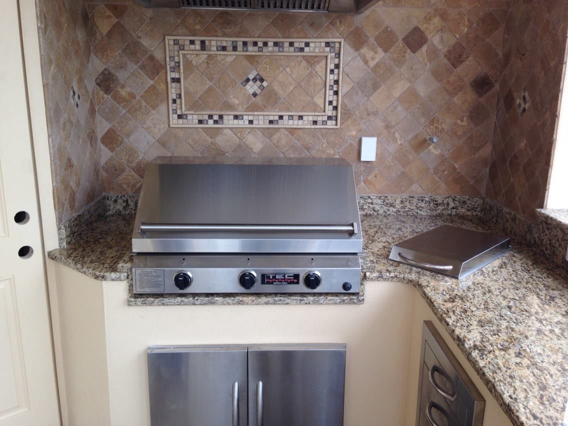 Outdoor kitchen with a stainless steel grill, cabinets, and granite countertops.
