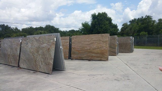 Large stone slabs, leaning against supports, outdoors in a yard. Cloudy sky with trees in the background.