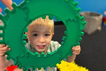 A little boy is holding a green gear in his hands