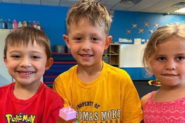 Three young children are posing for a picture in a classroom