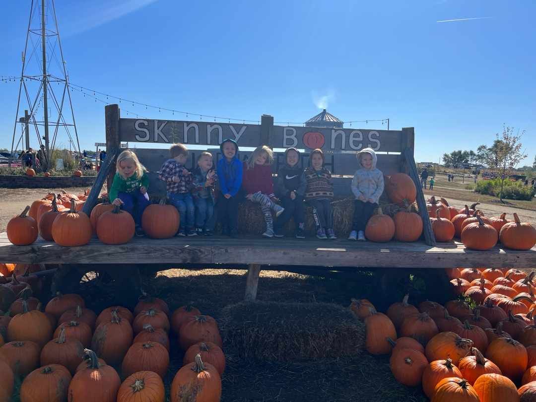 A group of children are sitting on a bench in a pumpkin patch