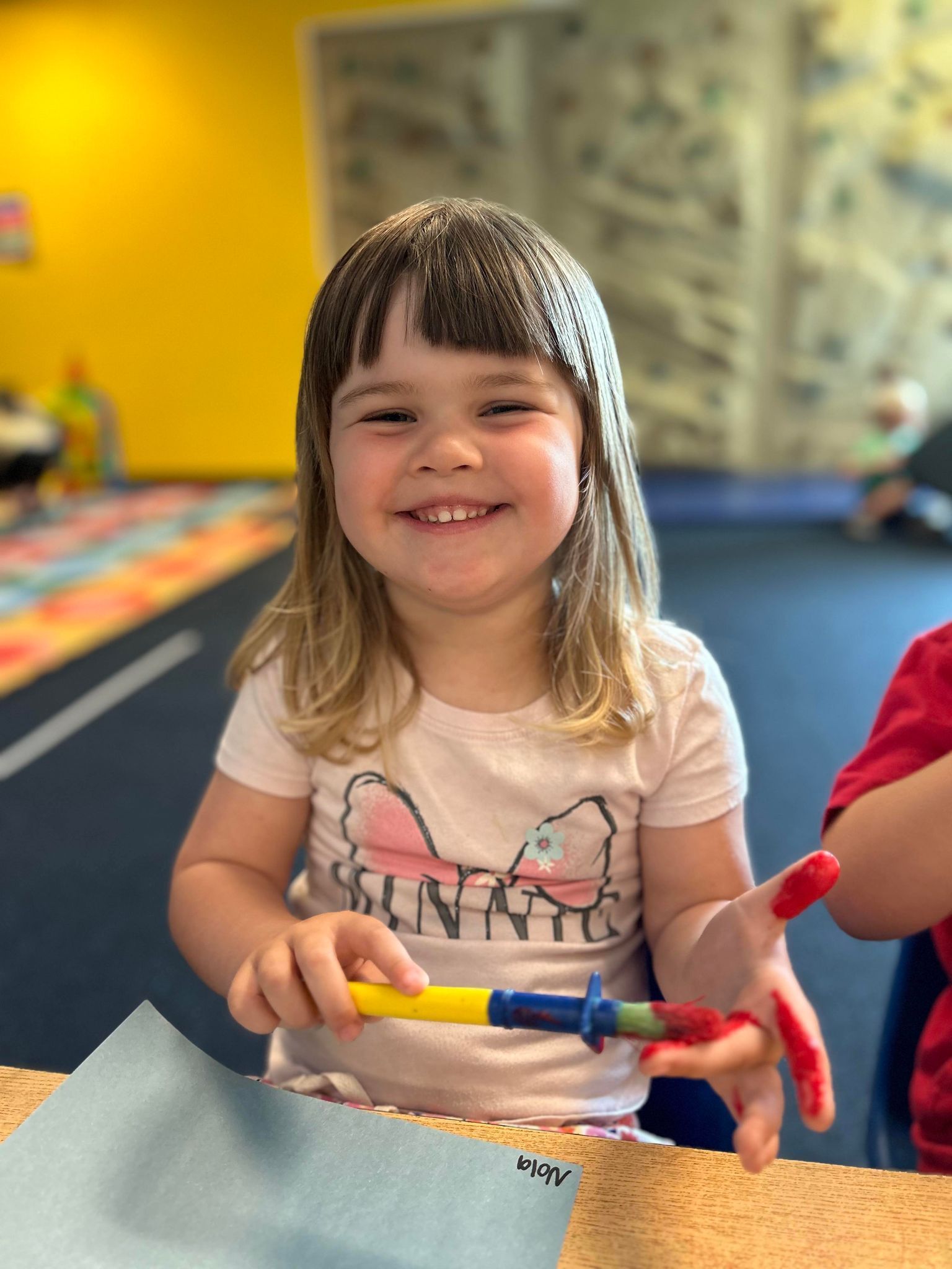 A little girl is smiling while holding a rainbow colored marker.